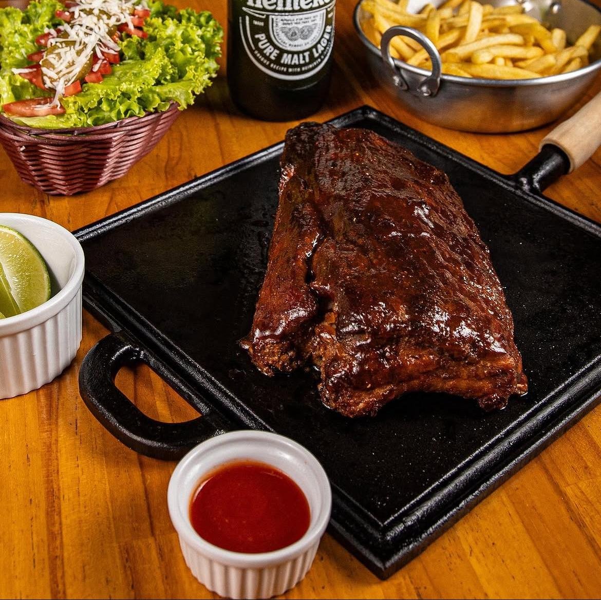 Costela ao barbecue na chapa quente, com salada, batata frita e cerveja